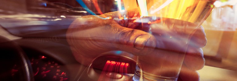 Person holding a glass of beer and blurry image of the dashboard of a car.