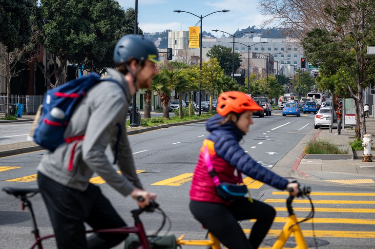 San Francisco 'overhauls' approach to tackling traffic violence Bicyclists peddling down a street in San Francisco with buildings and trees in the distance.