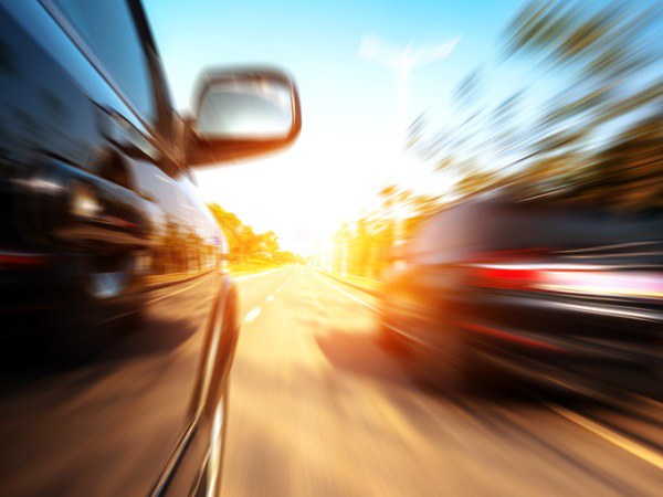 Speeding drivers Two black vehicles speeding by with trees on each side of the road.