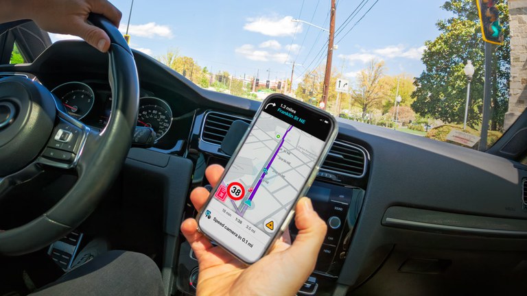 Using cellphones more when speeding Driver with one hand on the steering wheel and the other hand holding a cellphone with a navigation app showing directions.