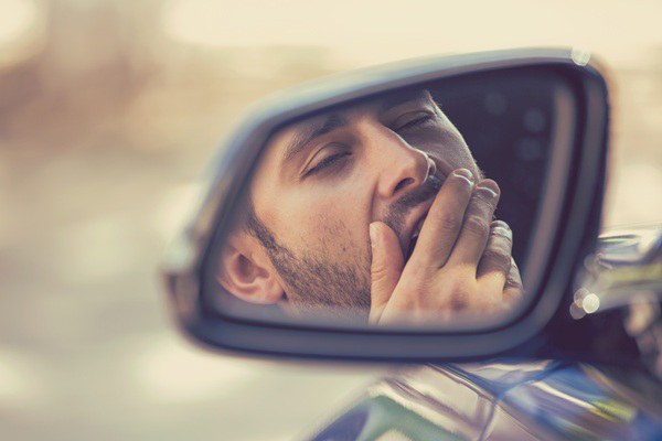 Reflection of a man yawning in the side mirror of a vehicle.