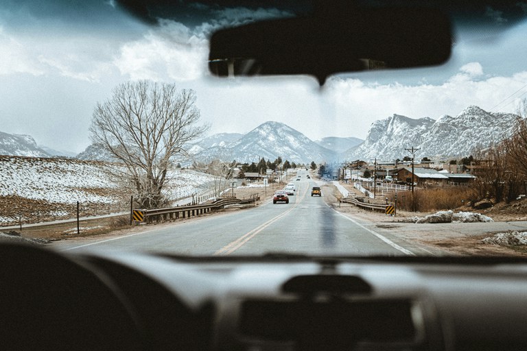 Cars driving down a rural Colorado road with snowy mountains in the distance.