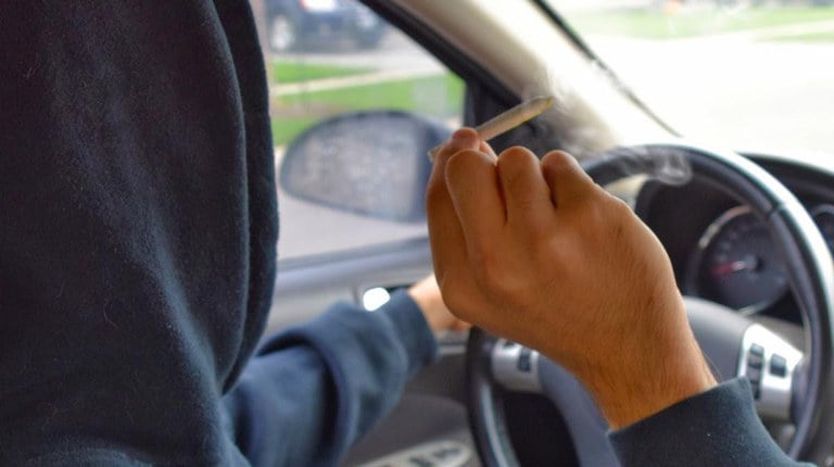 Person smoking cannabis behind the steering wheel of their car