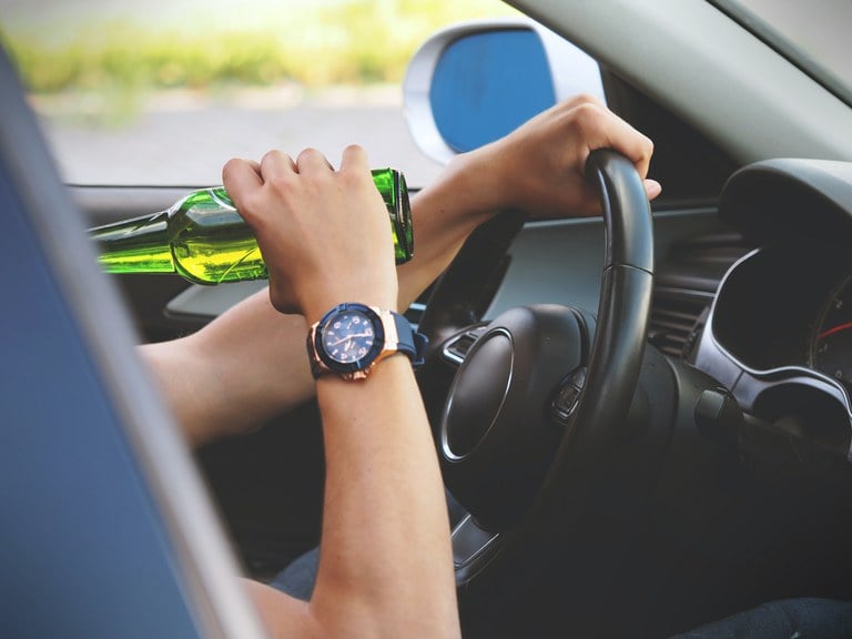 Person driving a car, one hand on the steering wheel and the other is holding a beer 