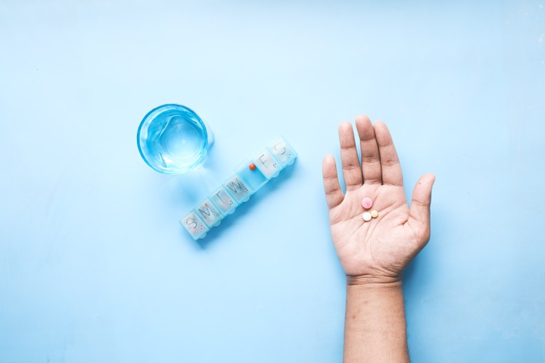 Pill organizer, glass of water and open palm with pills on a blue background