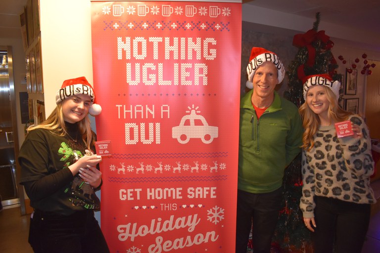 The Nothing Uglier Than a DUI Ugly Sweater Campaign event, 3 staffers stand around the campaign banner 