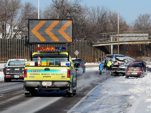 Emergency vehicle directing traffic past a motor crash on a snowy road.