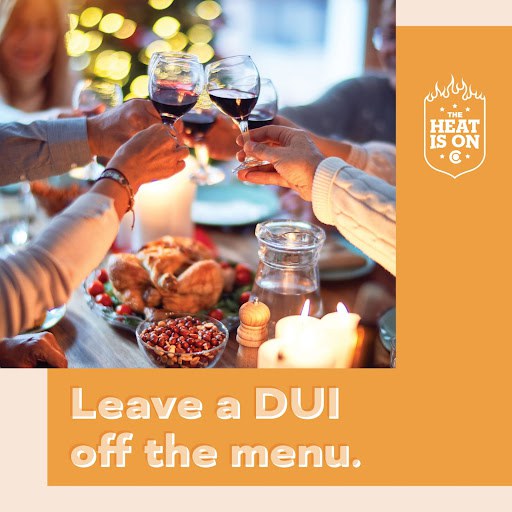 People at Thanksgiving dinner table cheers-ing red wine. Graphic copy reads “Leave  DUI off the menu.” The Heat is On logo in on the top right. 