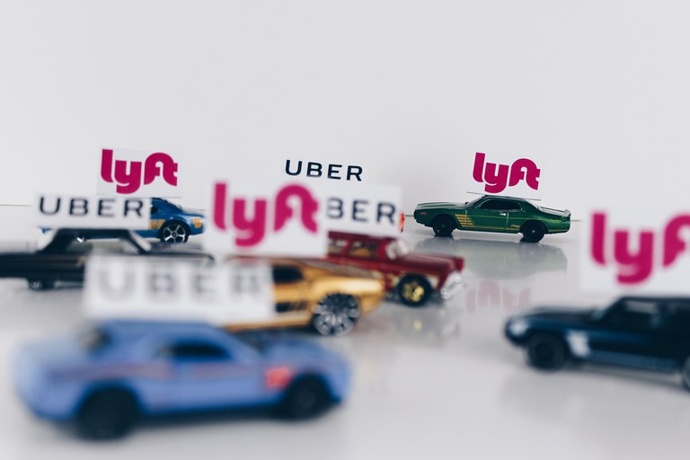 Eight toy cars with four Lyft and four Uber car topper banners on them. 