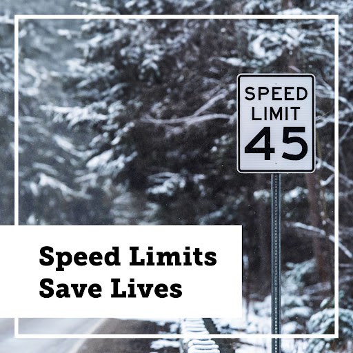 Alt text: A "speed limit 45" sign on the side of a snowy road. Snow-covered pines in the background. Text overlay reads "Speed Limits Save Lives"